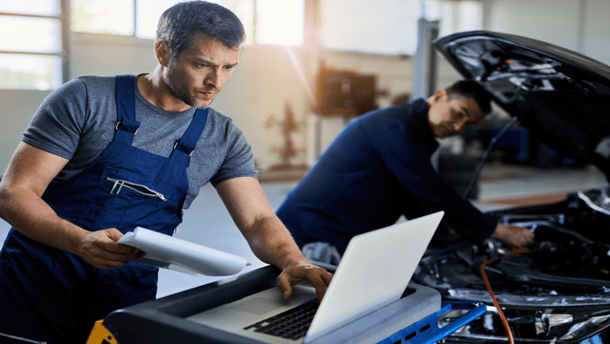 mecanico-adulto-medio-que-usa-una-computadora-portatil-para-el-diagnostico-del-automovil-mientras-trabaja-con-un-colega-en-el-taller-de-reparacion-de-automoviles